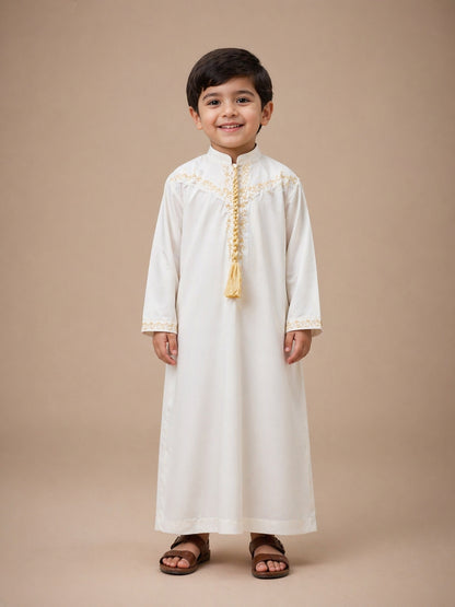 Child wearing a white Thobe Jubba traditional outfit with gold embroidery on a beige background